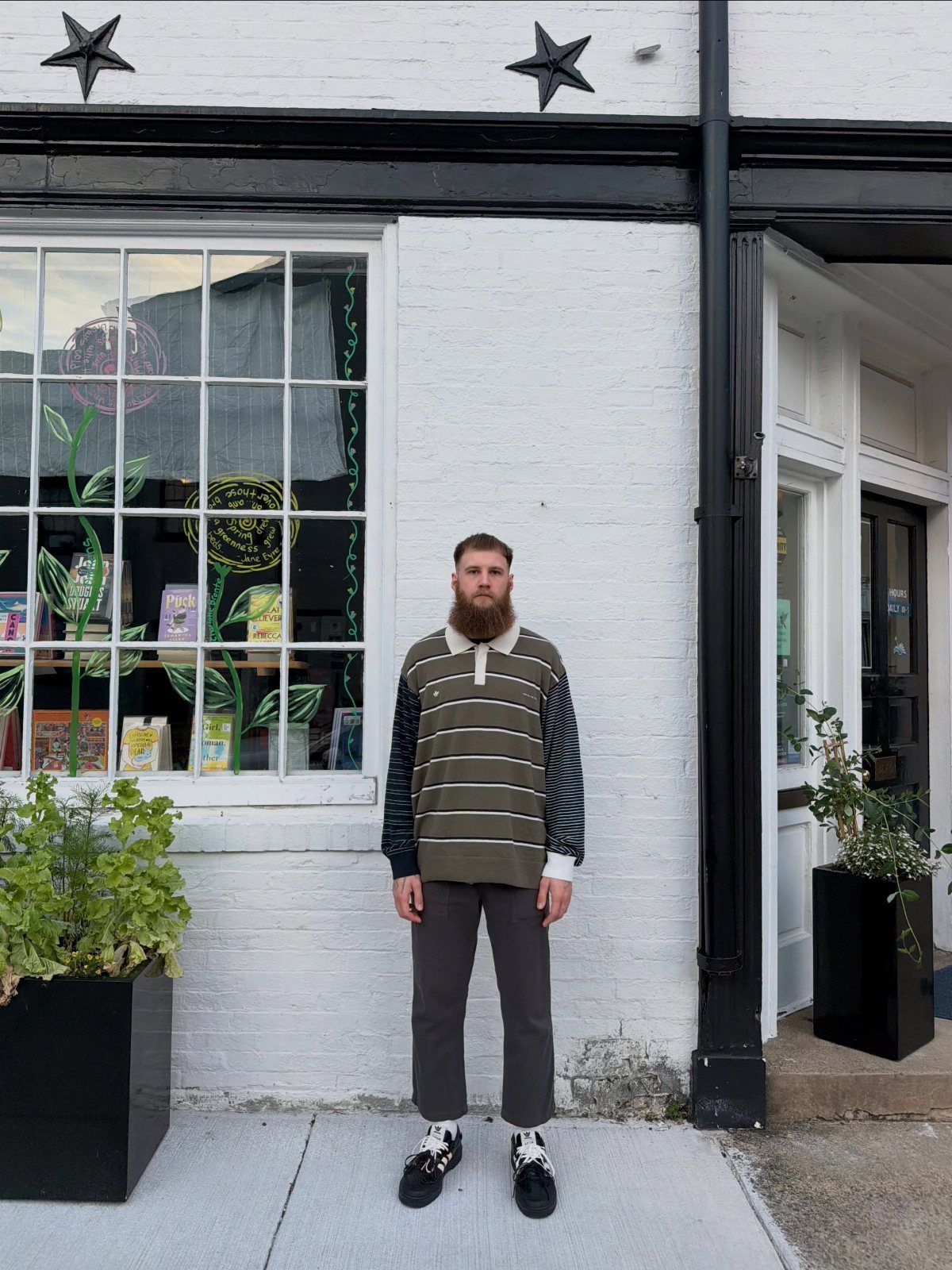 Man wearing a striped collared knit shirt and cuffed grey trousers with sneakers.