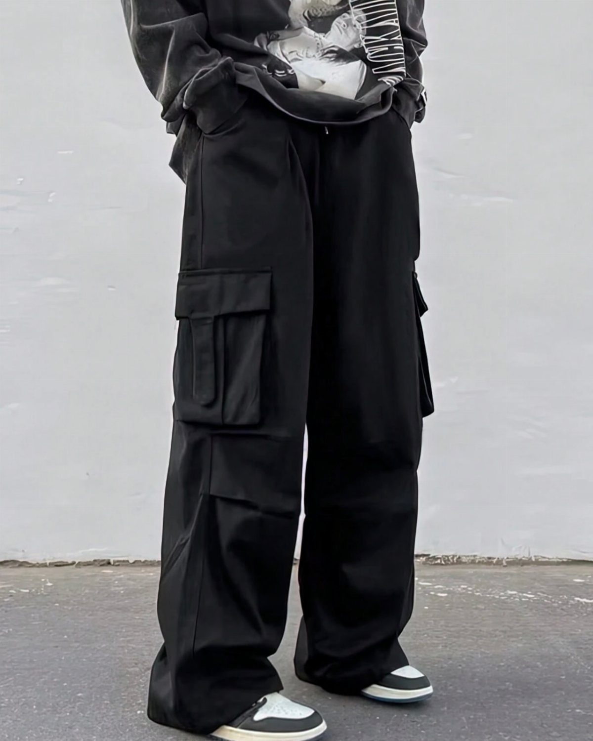 Person wearing oversized black cargo pants, a grey graphic tee, and sneakers.