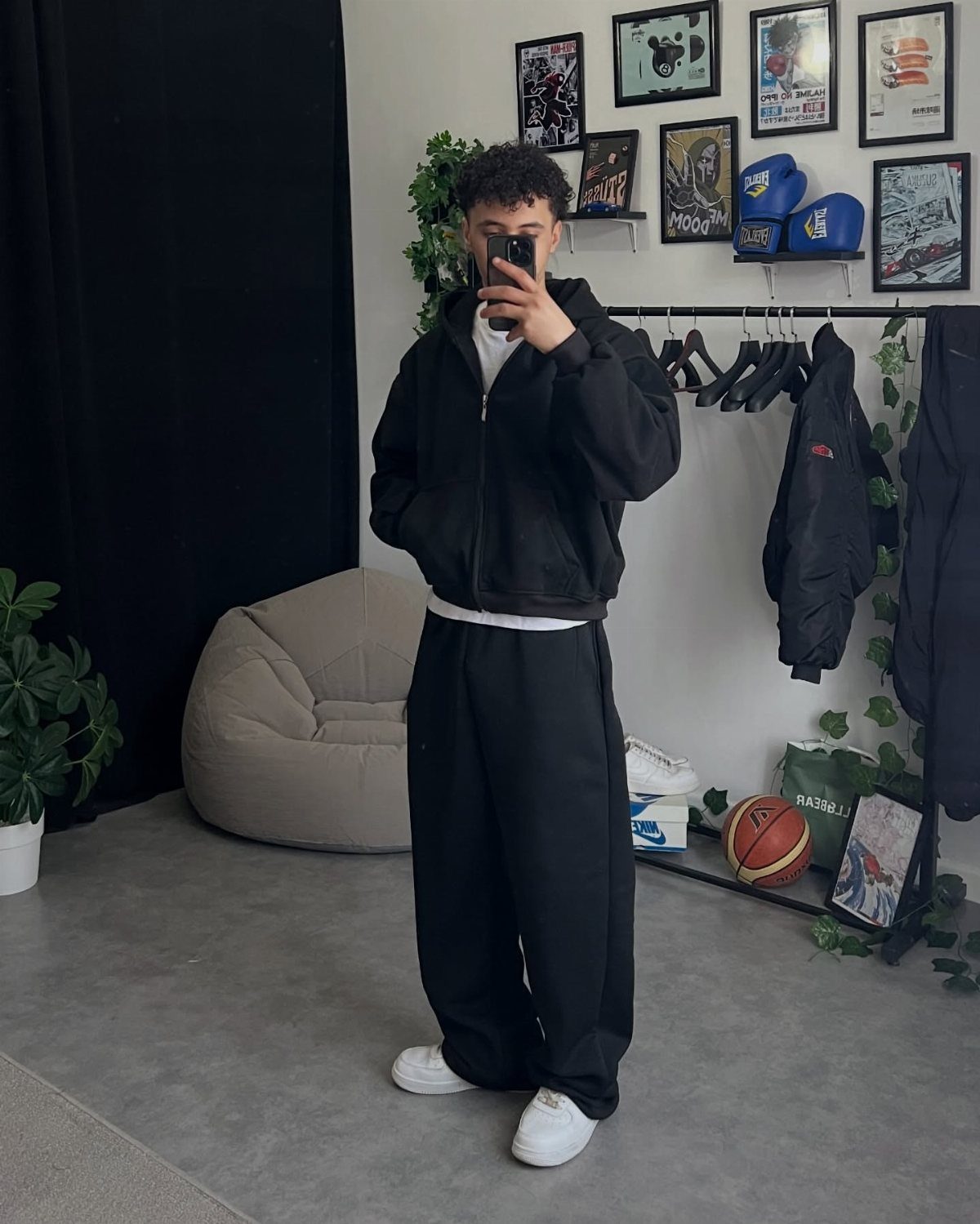 Person wearing baggy black sweatpants, a black jacket, and white sneakers in a room.