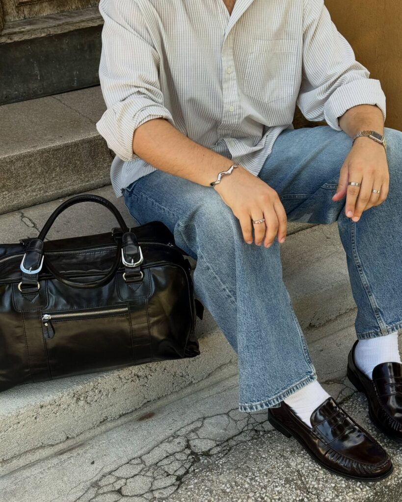 Person wearing a striped shirt, blue jeans, and dark leather loafers sitting on steps.