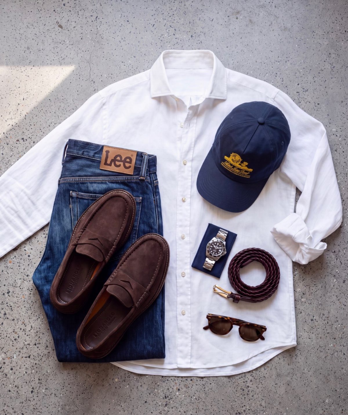 Brown suede loafers arranged with a white shirt, blue jeans, and navy cap.