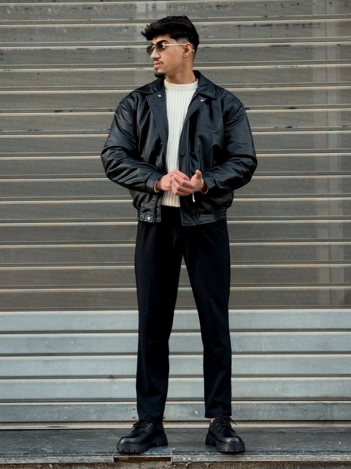Man wearing black leather jacket, white sweater, black trousers, and chunky black derby shoes.