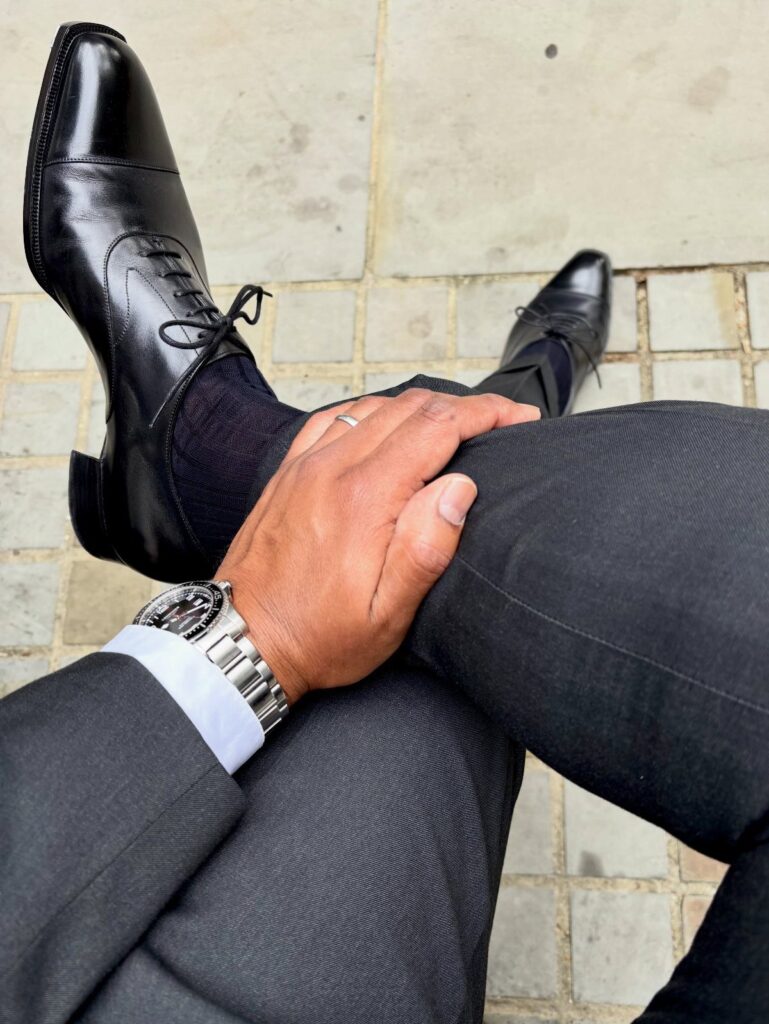 Polished black leather Oxford shoes worn with a grey suit and black socks.