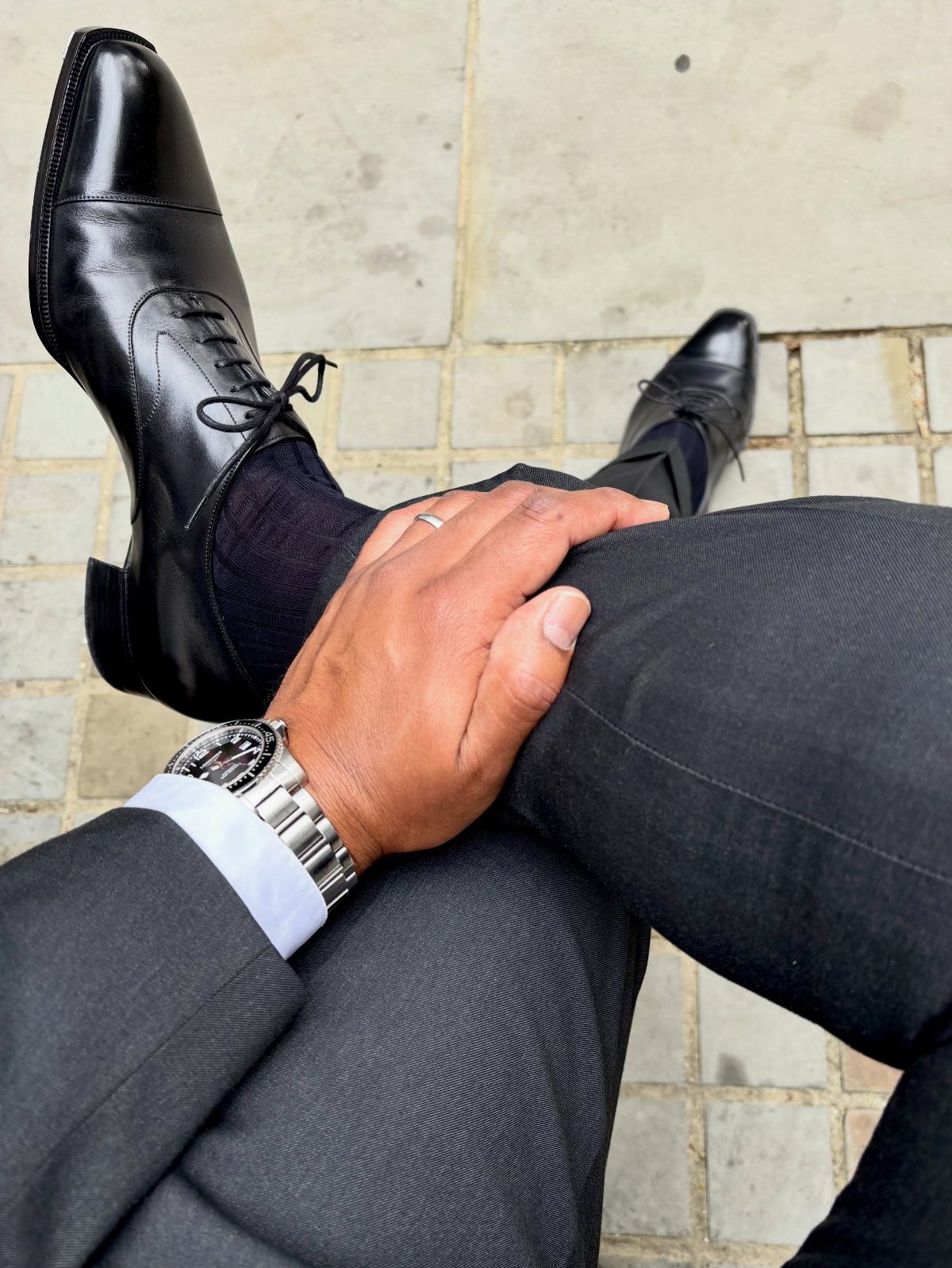 Polished black leather Oxford shoes worn with a grey suit and black socks.