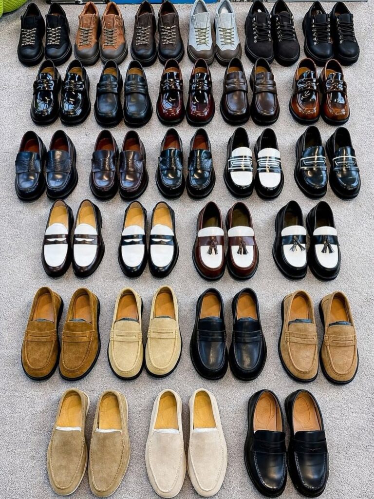 Various men's dress shoes in leather and suede arranged in rows on carpet.