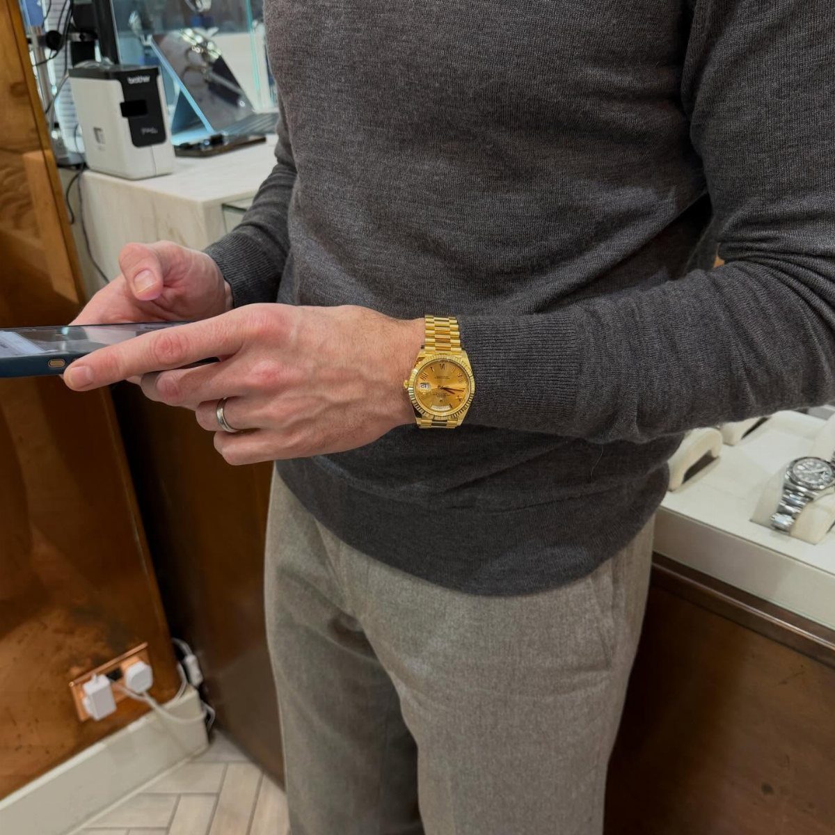 Man wearing a grey sweater and trousers with a gold watch on wrist