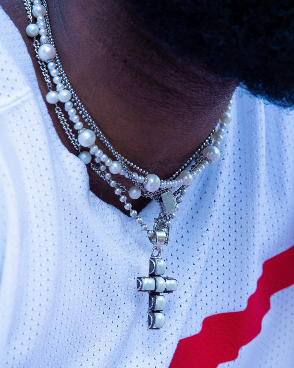 Layered pearl and silver chain necklaces with a cross pendant on a man