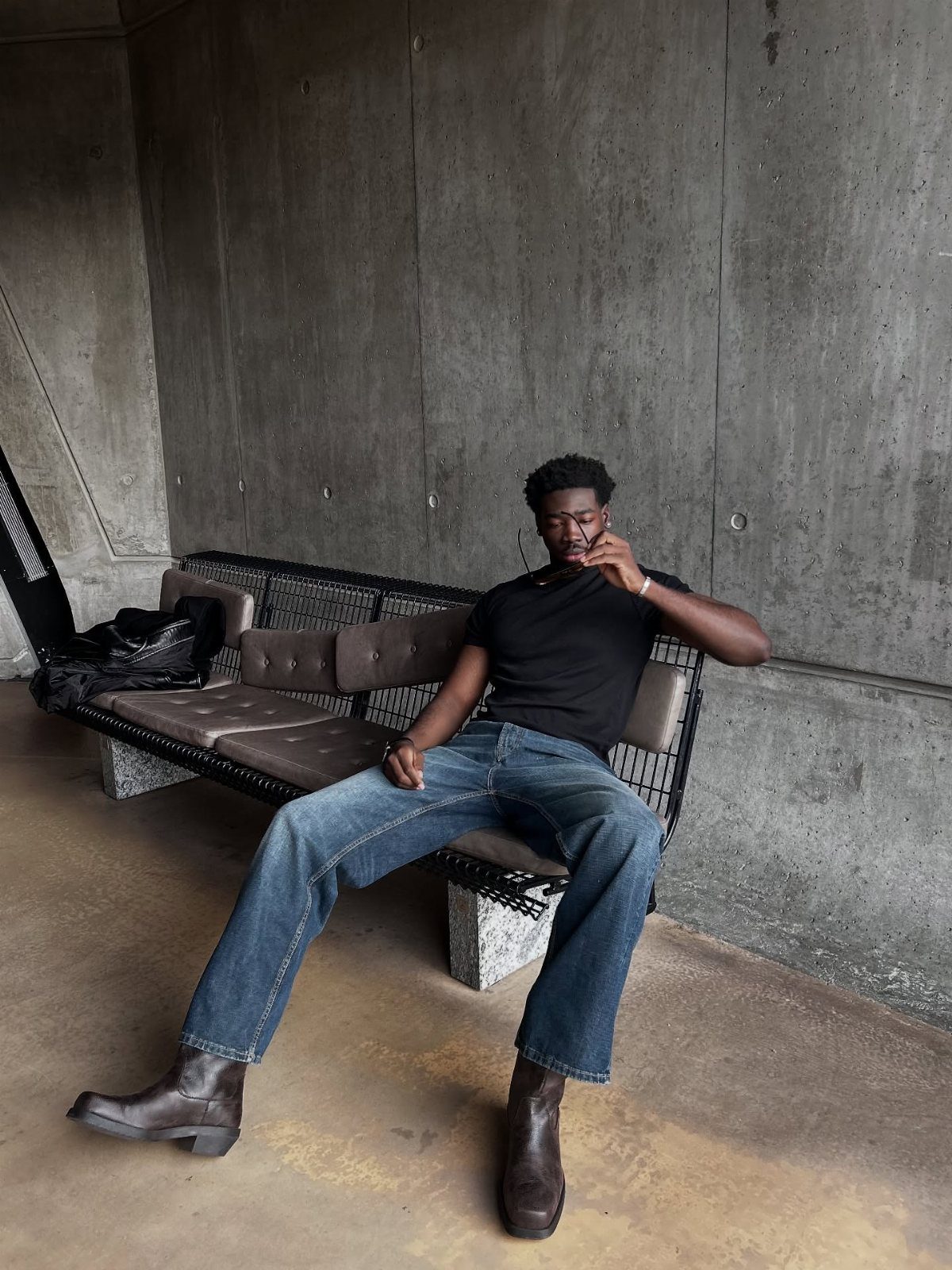 Man wearing dark brown Chelsea boots and blue jeans sitting on a bench.