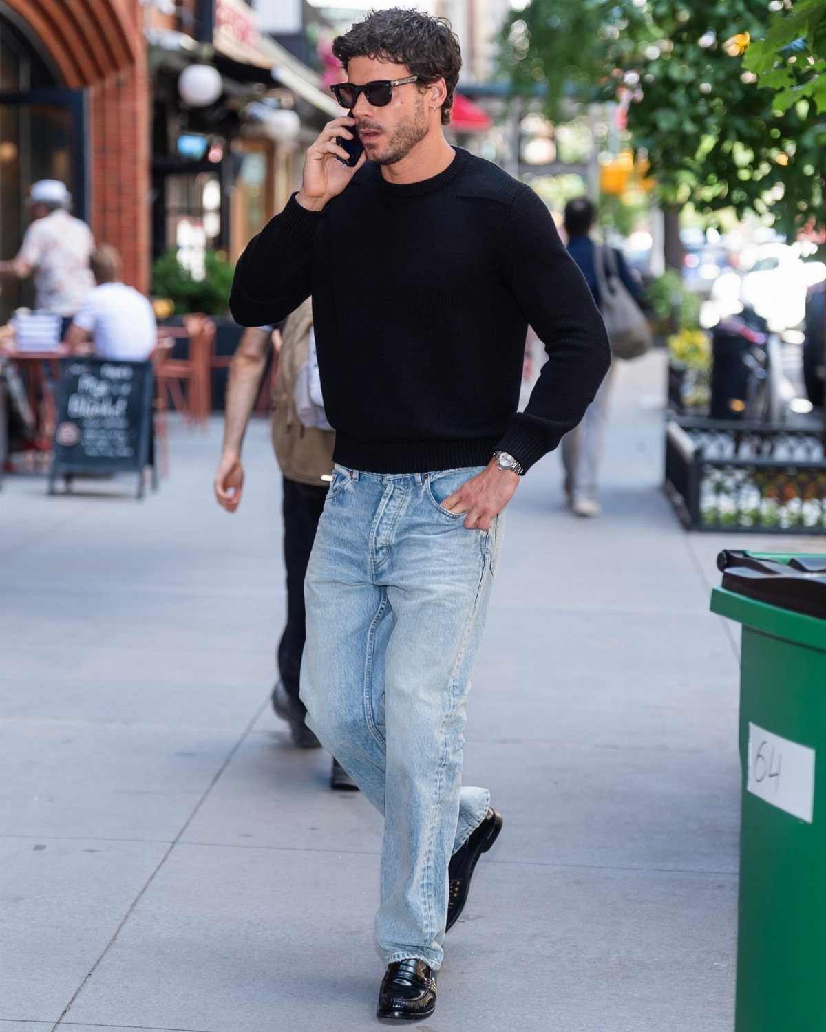 Man in black sweater and light blue jeans wearing black leather loafers walking outdoors