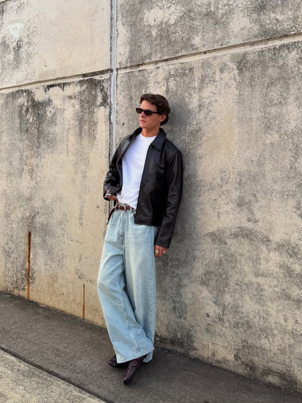 Man in black leather jacket, white t-shirt, and light blue wide-leg jeans.