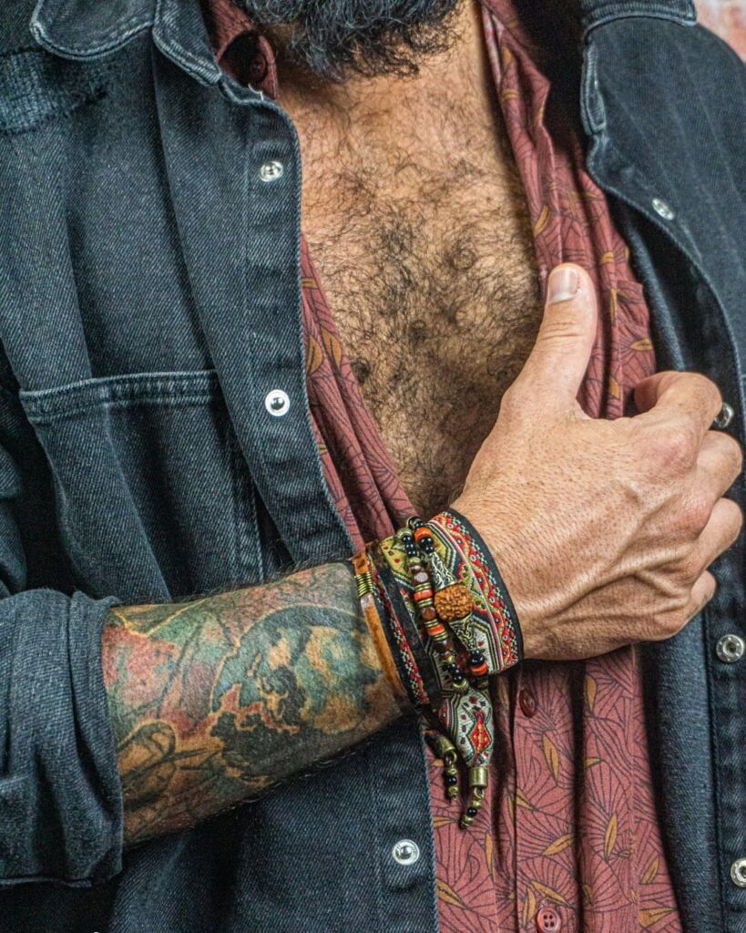 Tattooed forearm wearing a stack of beaded and braided cord bracelets.