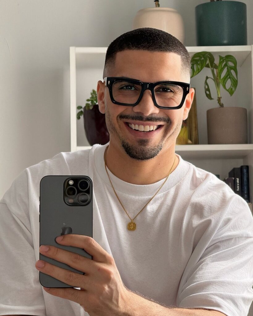 Smiling man wearing oversized black rectangular glasses and a white t-shirt.