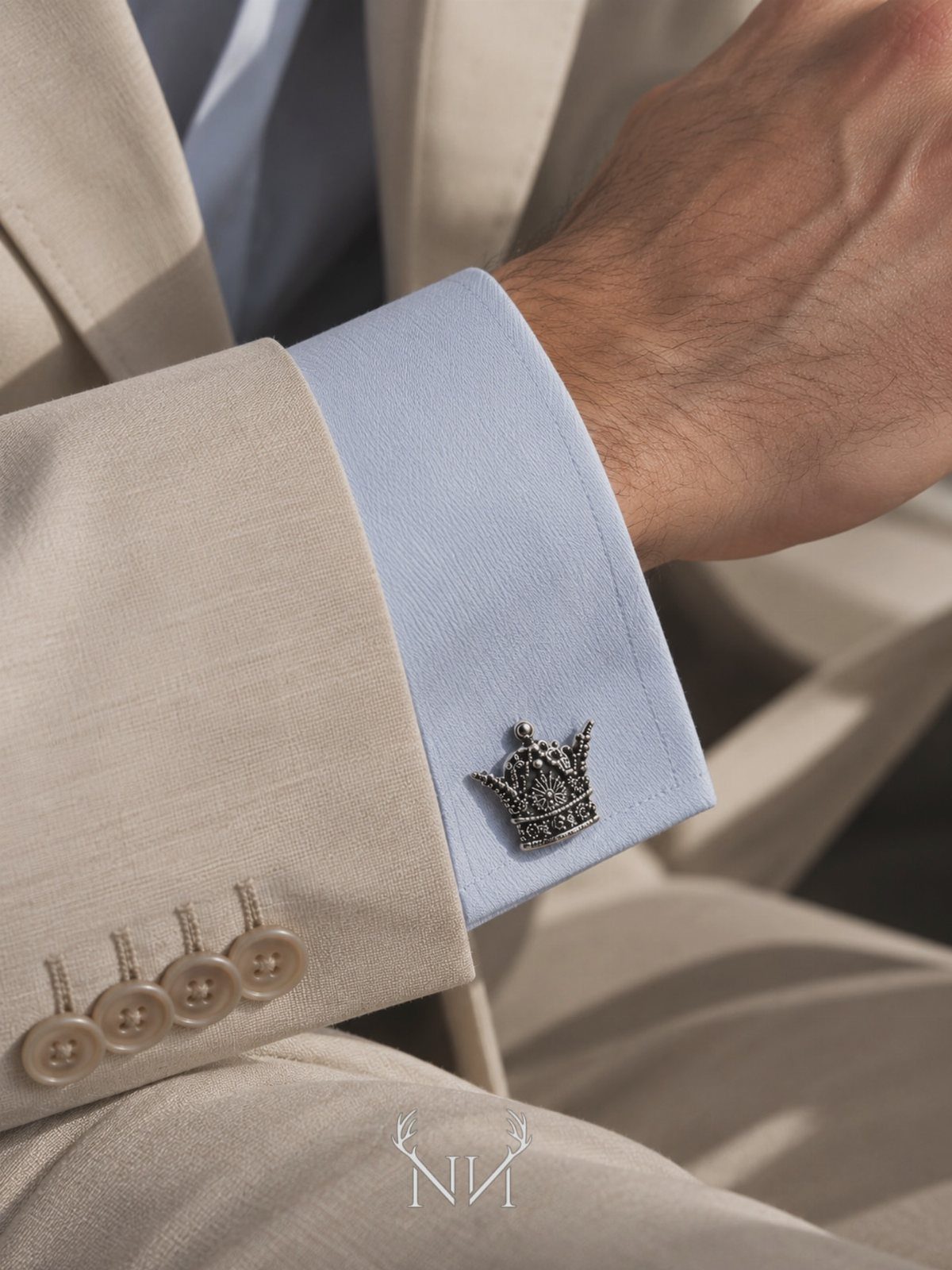 Silver crown cufflink on a light blue dress shirt and beige suit jacket sleeve