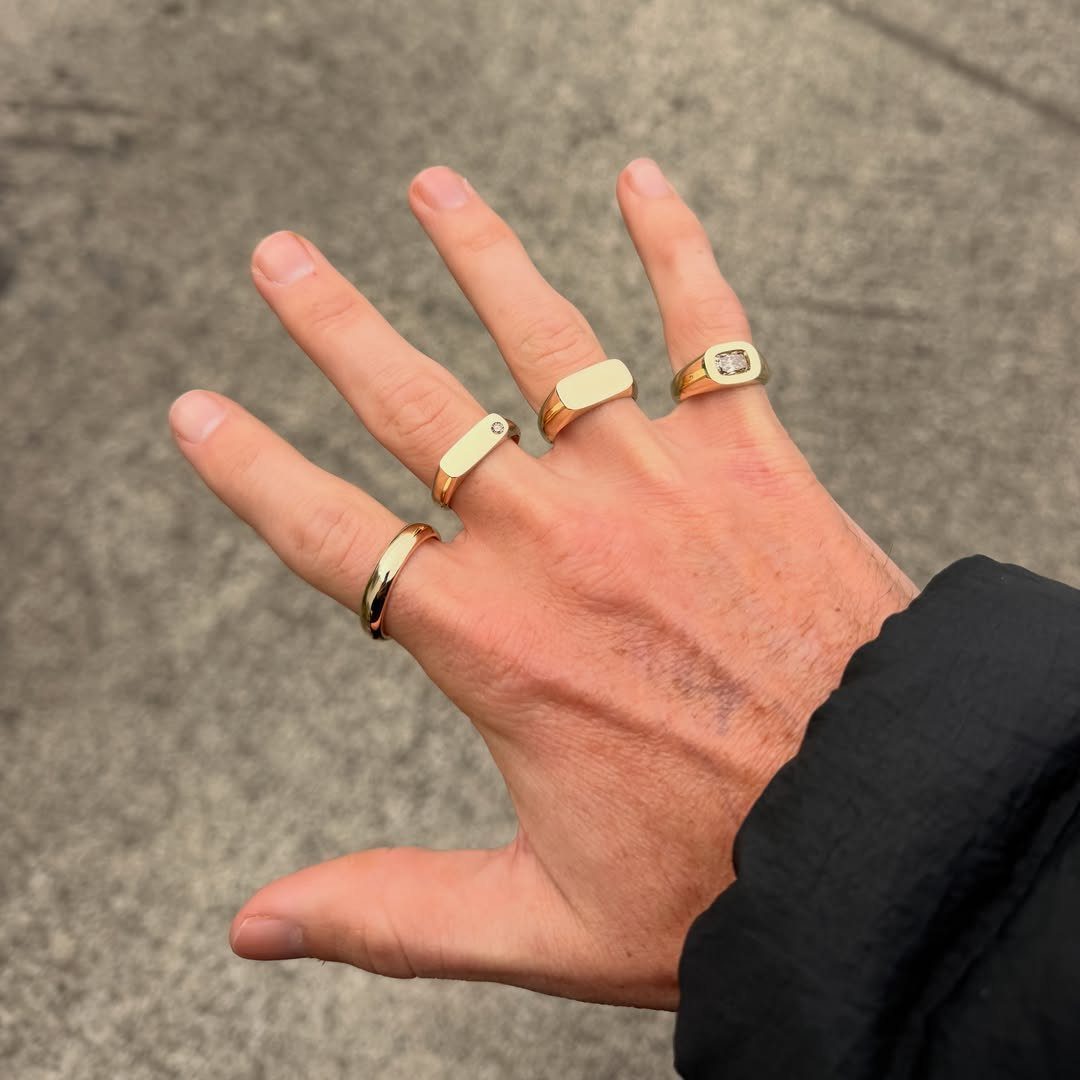 Man's hand wearing four different gold rings against a grey concrete background