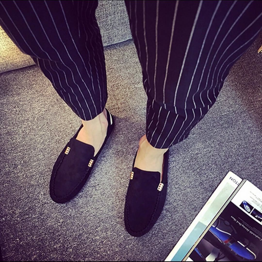 Black suede driving shoes with gold accents worn with navy pinstriped trousers.