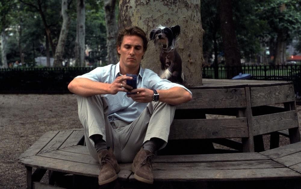 Man wearing brown suede desert boots sitting on a wooden park bench with dog.