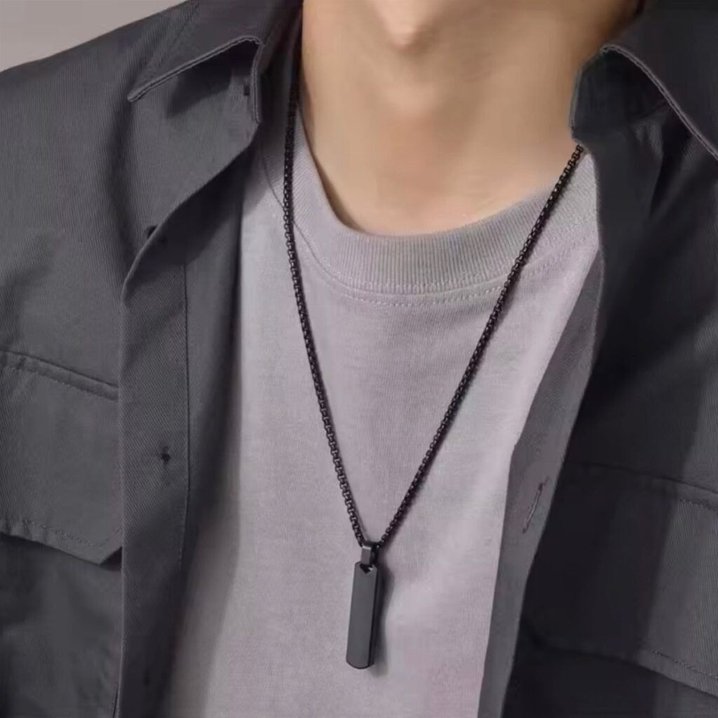 Man wearing a black chain necklace with a rectangular pendant over grey clothing