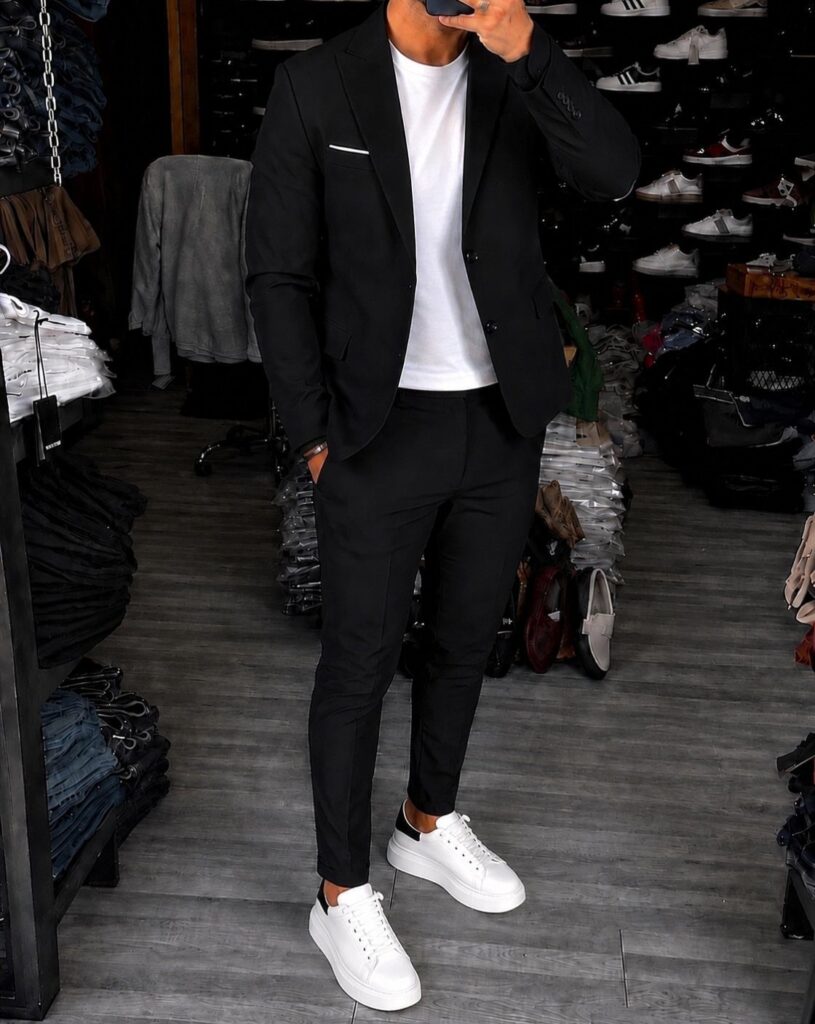 Man wearing a black blazer and trousers with a white t-shirt and white sneakers.
