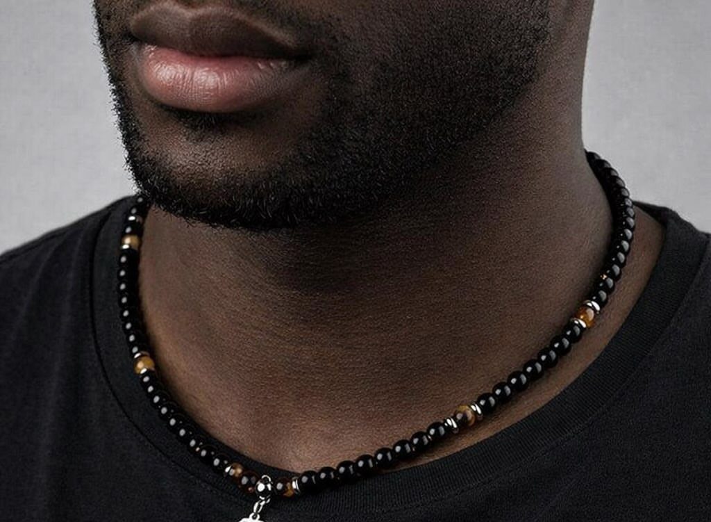 Black beaded necklace with brown accents and silver pendant on a man's neck.