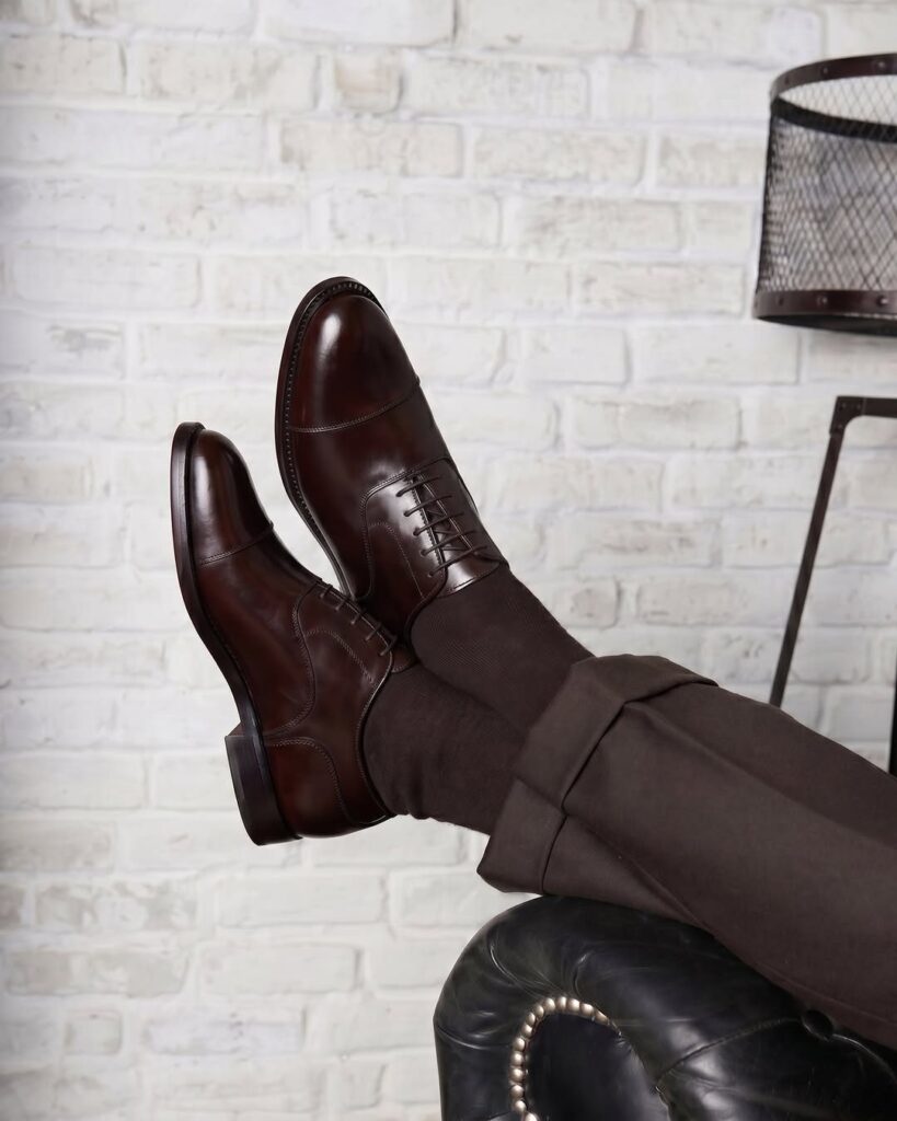 Dark brown leather oxford shoes paired with brown trousers and socks.