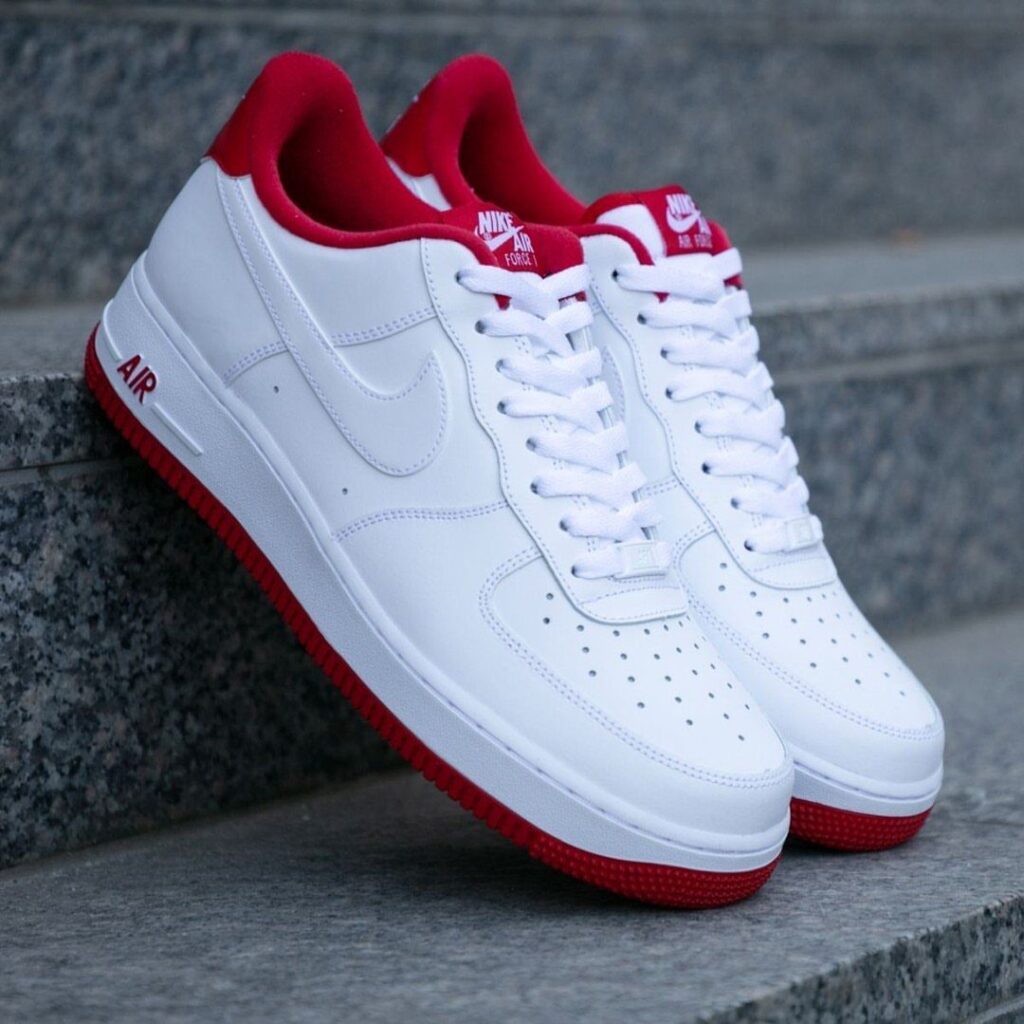 White leather sneakers with red soles and linings on grey stone steps