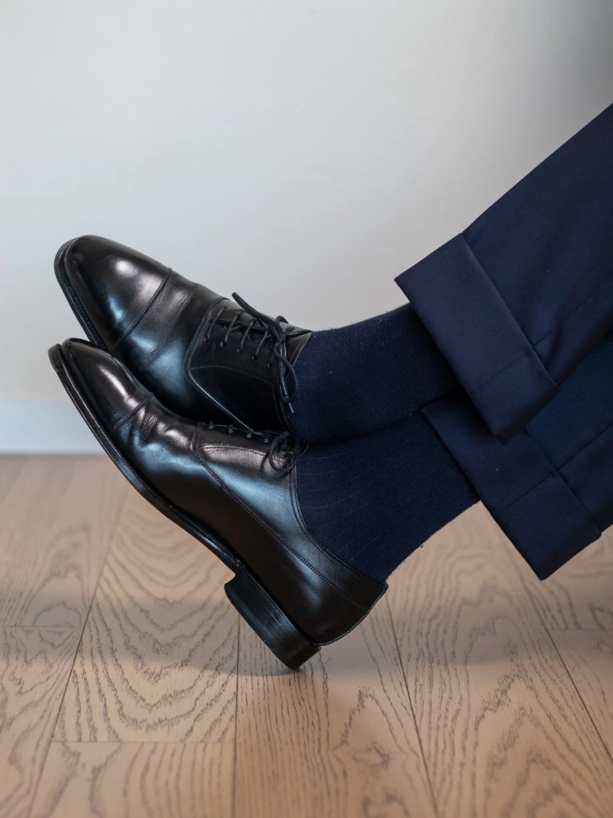 Polished black leather oxford shoes paired with navy blue suit trousers and socks.