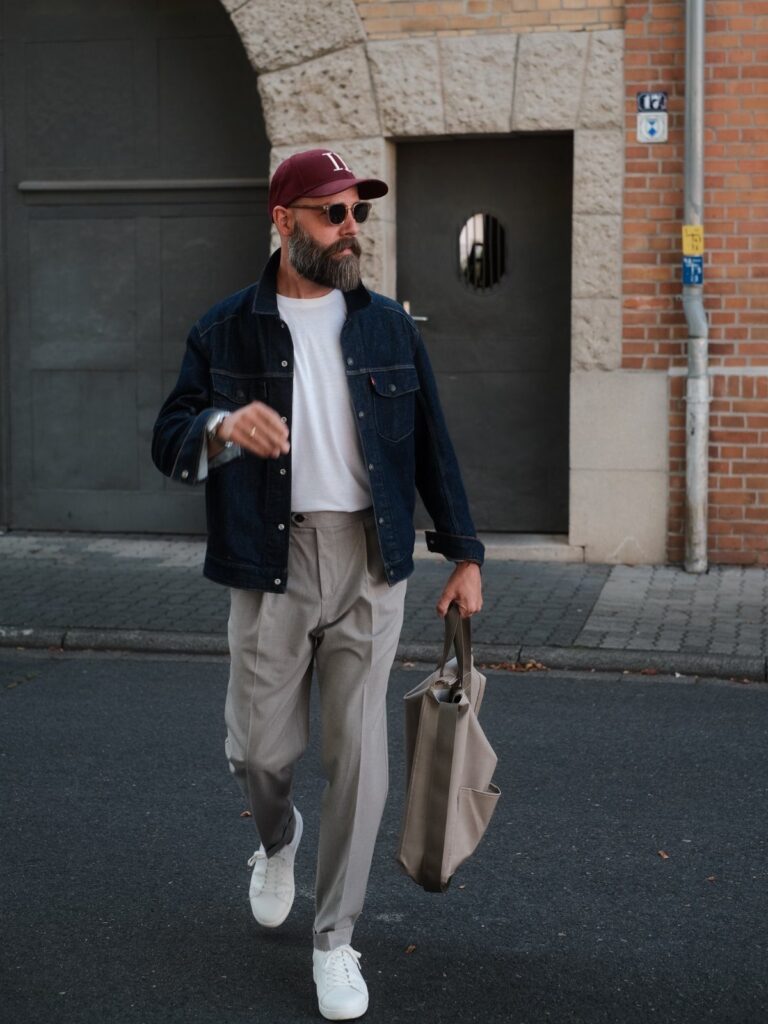 Man in denim jacket and tailored grey trousers wearing white minimal sneakers.