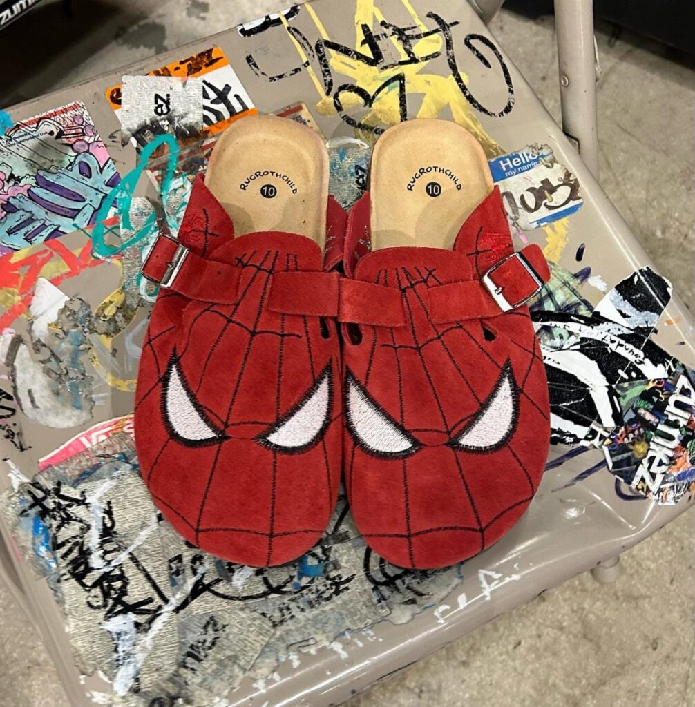Red Spider-Man themed suede clogs with web patterns and white eyes on a tray.
