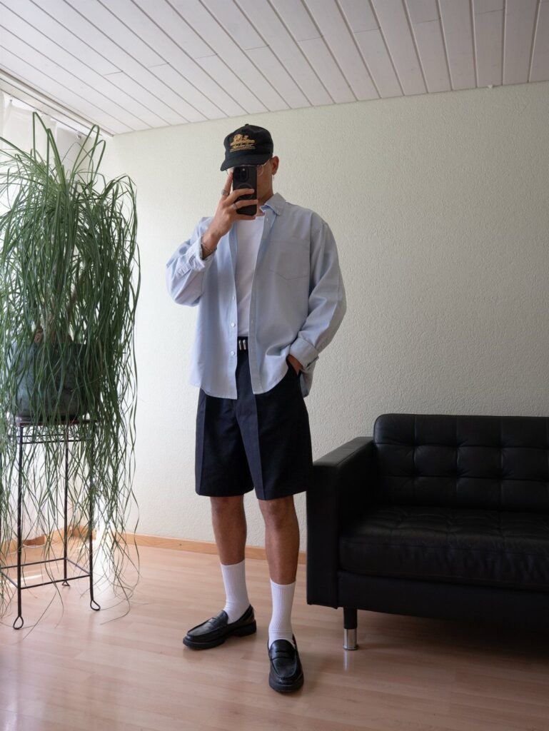 Man wearing black loafers with black shorts, white socks, and a light blue shirt.