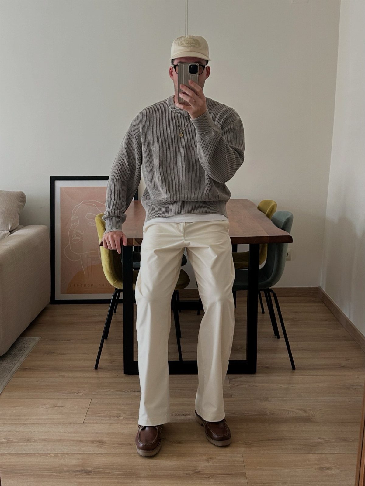 Man wearing a grey sweater, white pants, and brown boat shoes in a room.
