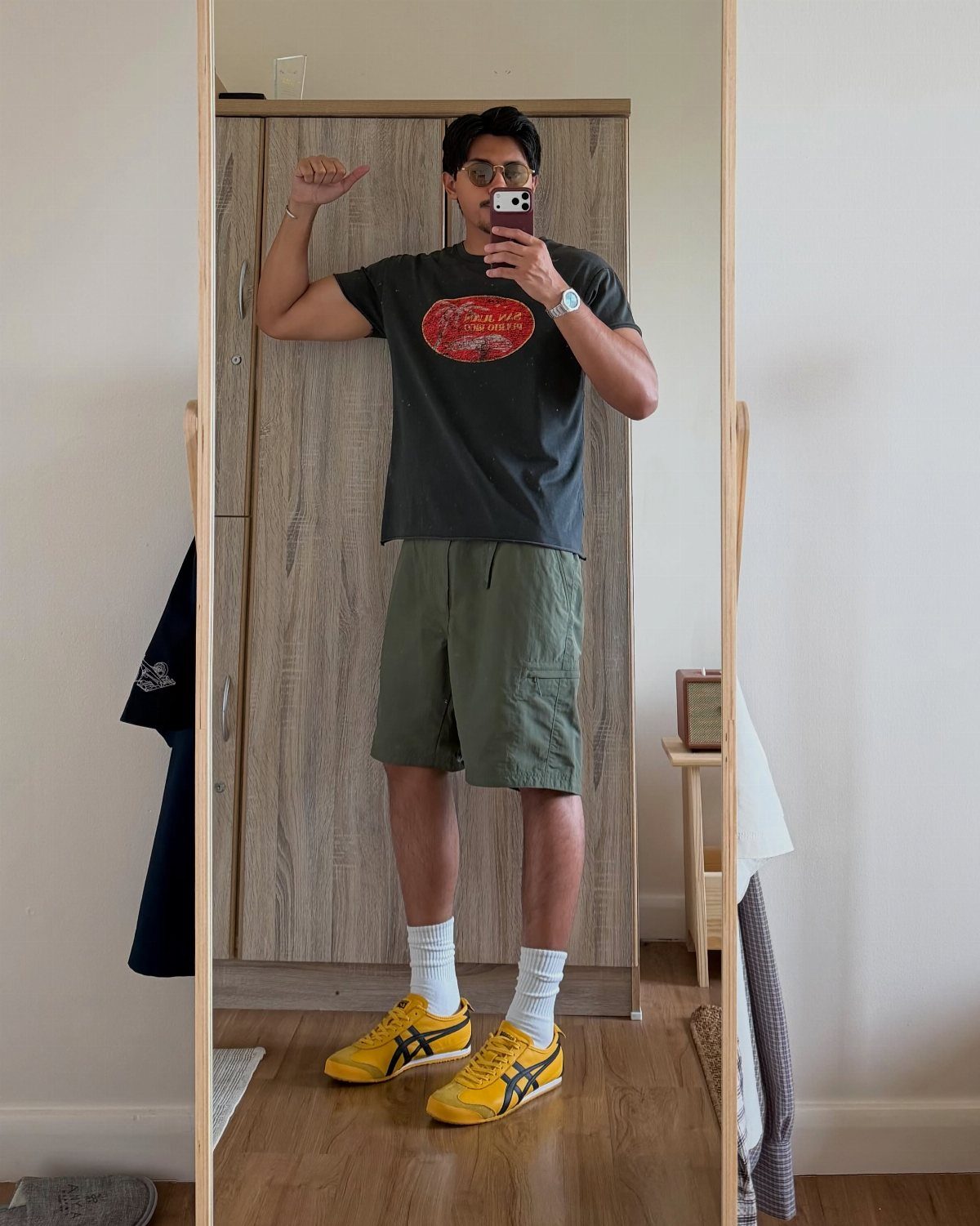 Man in olive shorts and yellow Onitsuka Tiger sneakers taking a mirror selfie.