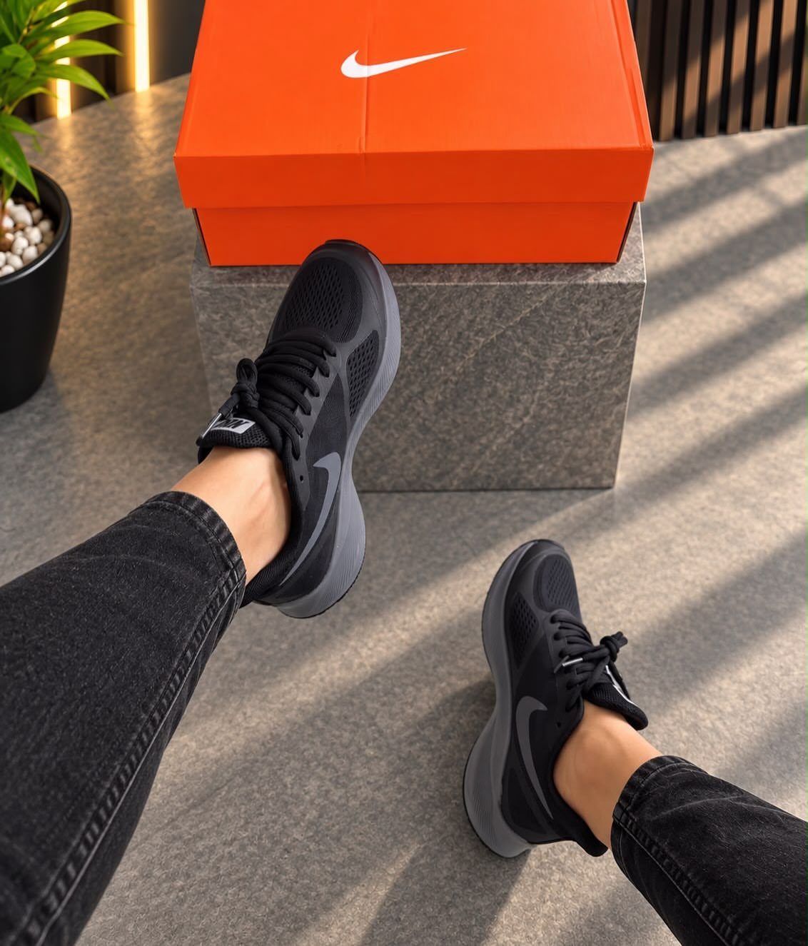 Black Nike sneakers worn with black jeans next to an orange shoebox.