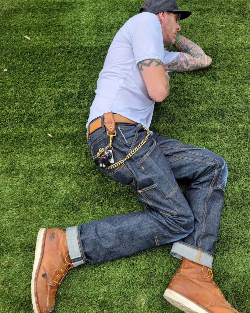 Man in white t-shirt and dark denim jeans wearing brown leather boots.