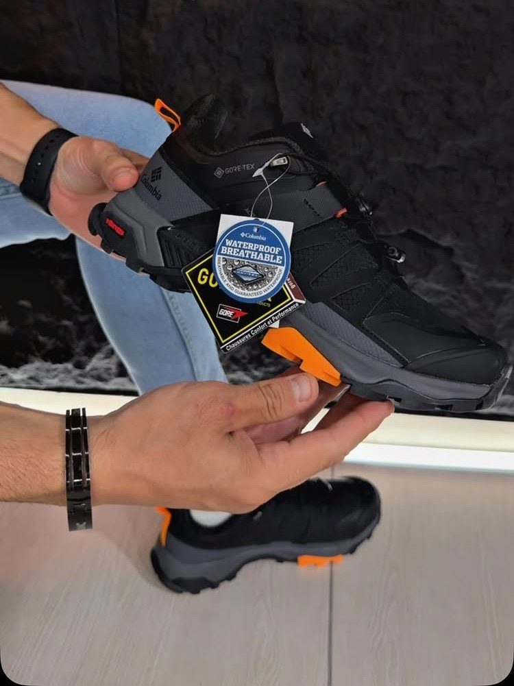 Black and grey waterproof sneaker with orange accents held by two hands.