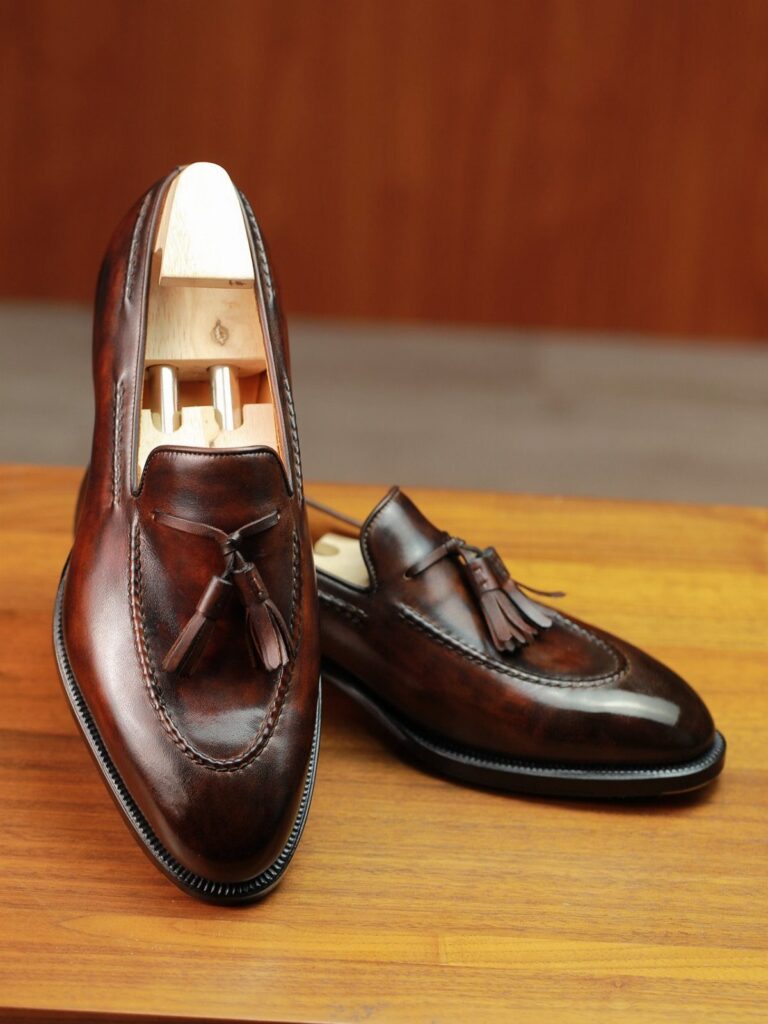 Dark brown leather tassel loafers with polished finish on a wooden table.