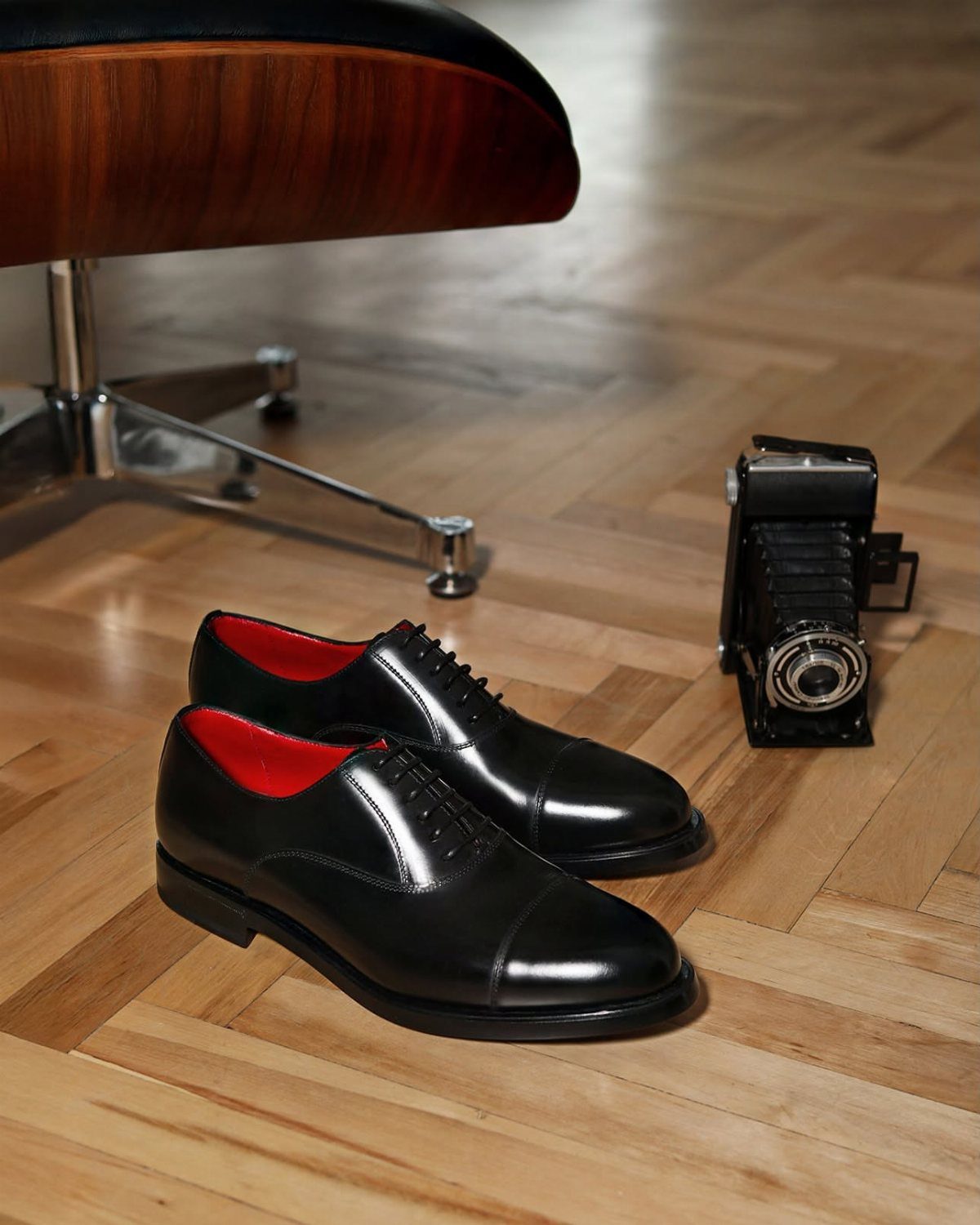 Black leather Oxford shoes with red lining on a herringbone wood floor