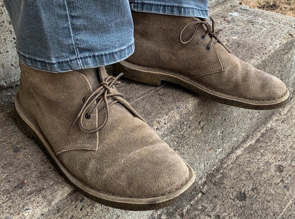 Brown suede chukka boots worn with blue jeans on a concrete step.