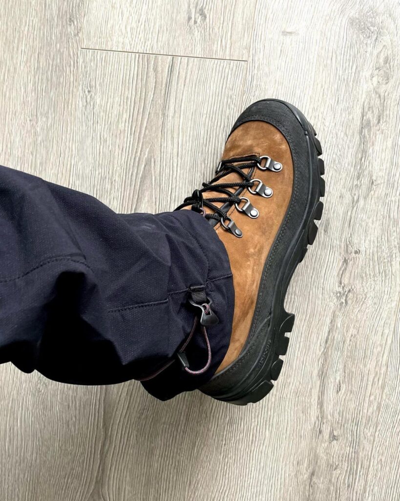 Brown suede hiking boot with chunky black soles on a light wood floor.